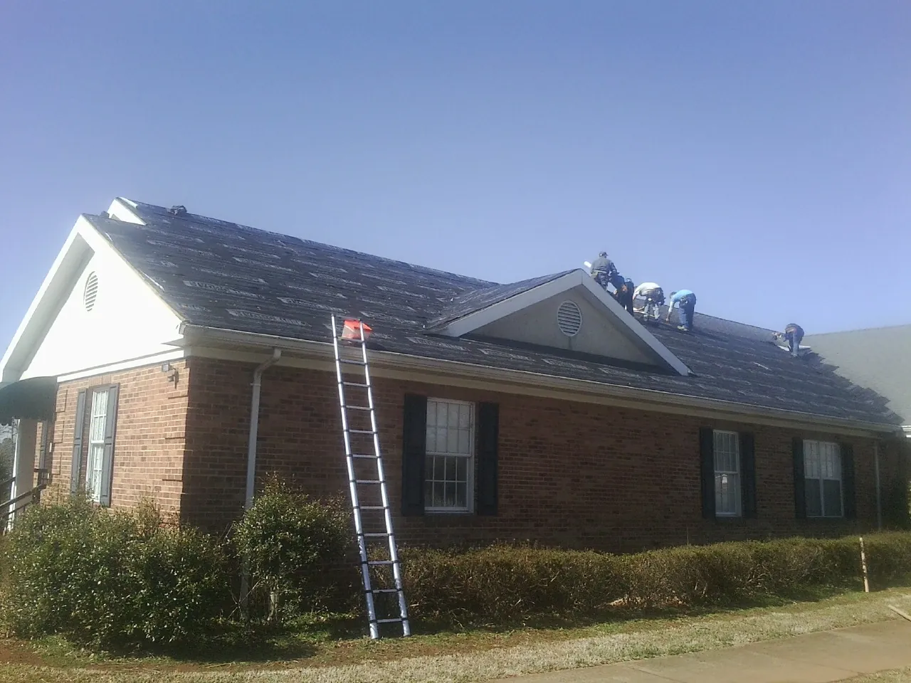 Crew tearing shingles off a brick ranch roof with a ladder set — Metal Roof Repair work by our crew in Kennedy