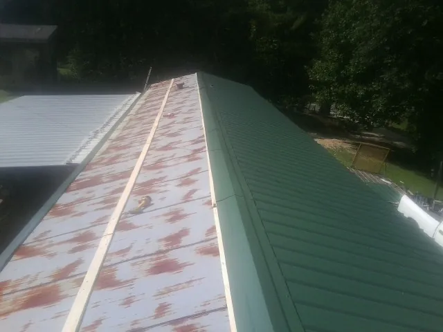 Old rusted panels beside newly installed green metal roofing — Wind Damage Roof Repair by Roofing Brothers in Kennedy