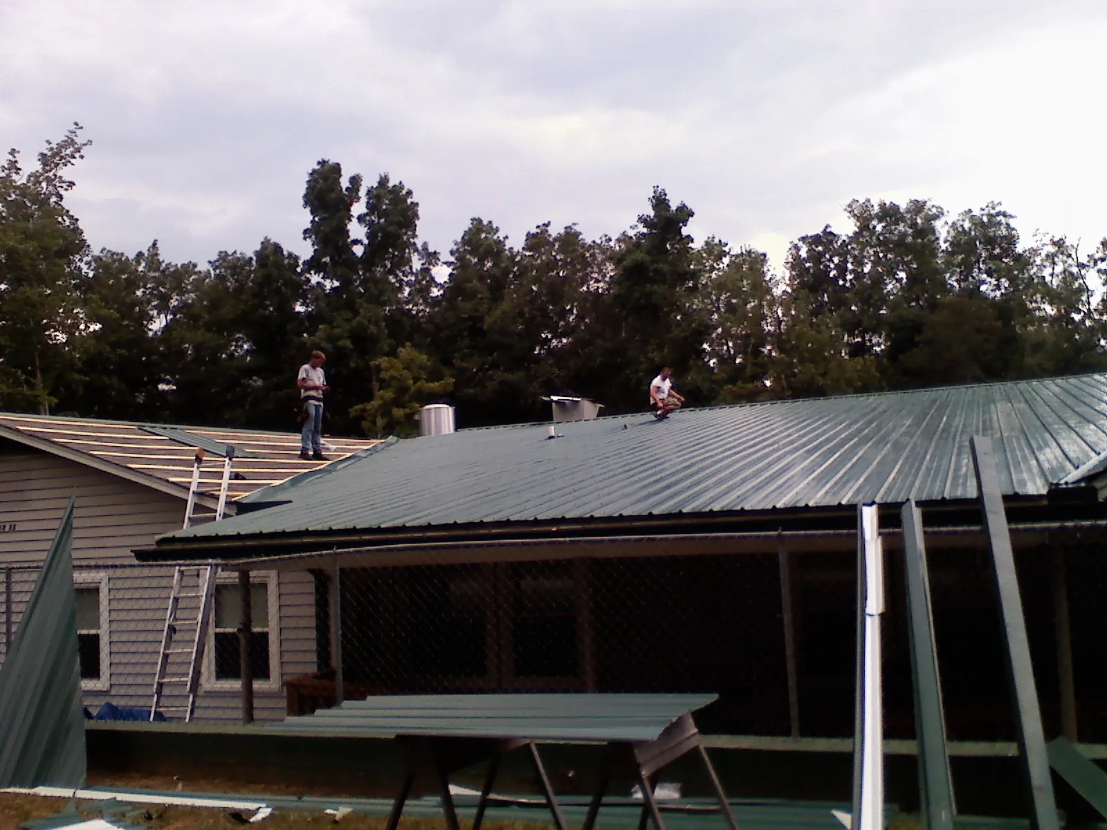 Two roofers installing green metal panels above a covered porch in Kennedy
