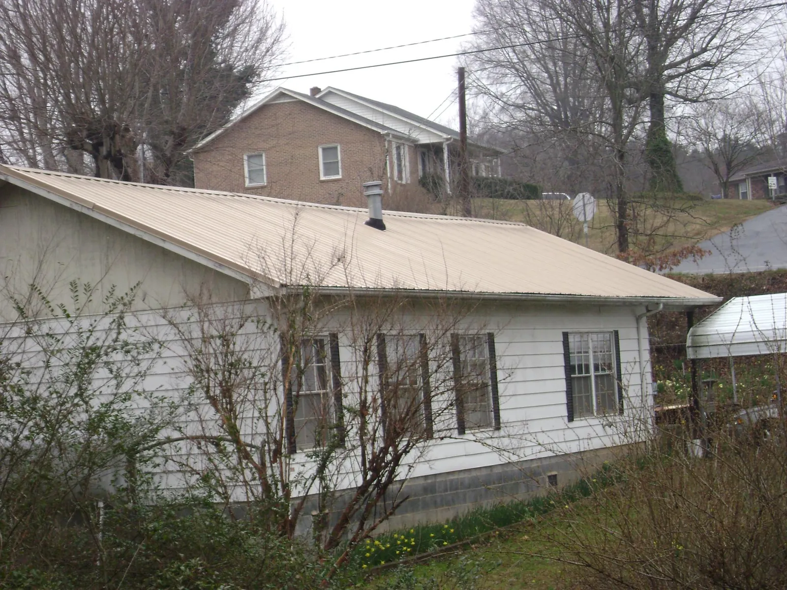 Tan metal roof on a white sided house set into a hillside — Commercial Roofing by Roofing Brothers in Kennedy